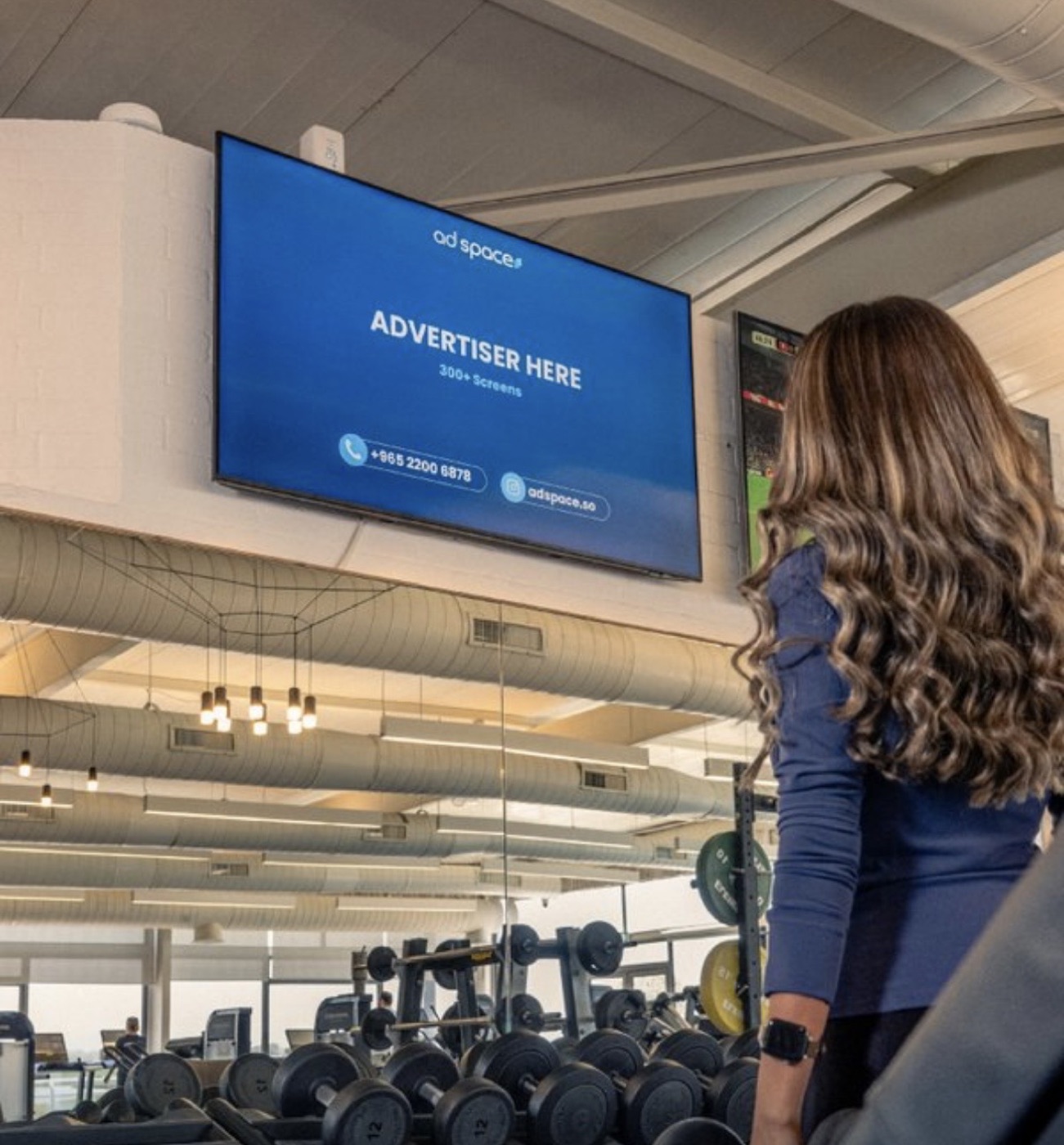 An Ad Space screen above the weights floor of a gym in Kuwait